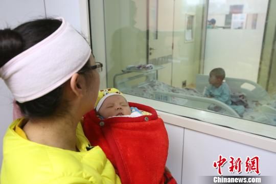 安安妈妈抱着刚满月的妹妹焦急地等待在层流仓外,凝视着移植手术的全过程。 周磊 摄 安安妈妈抱着刚满月的妹妹焦急地等待在层流仓外,凝视着移植手术的全过程。 周磊 摄